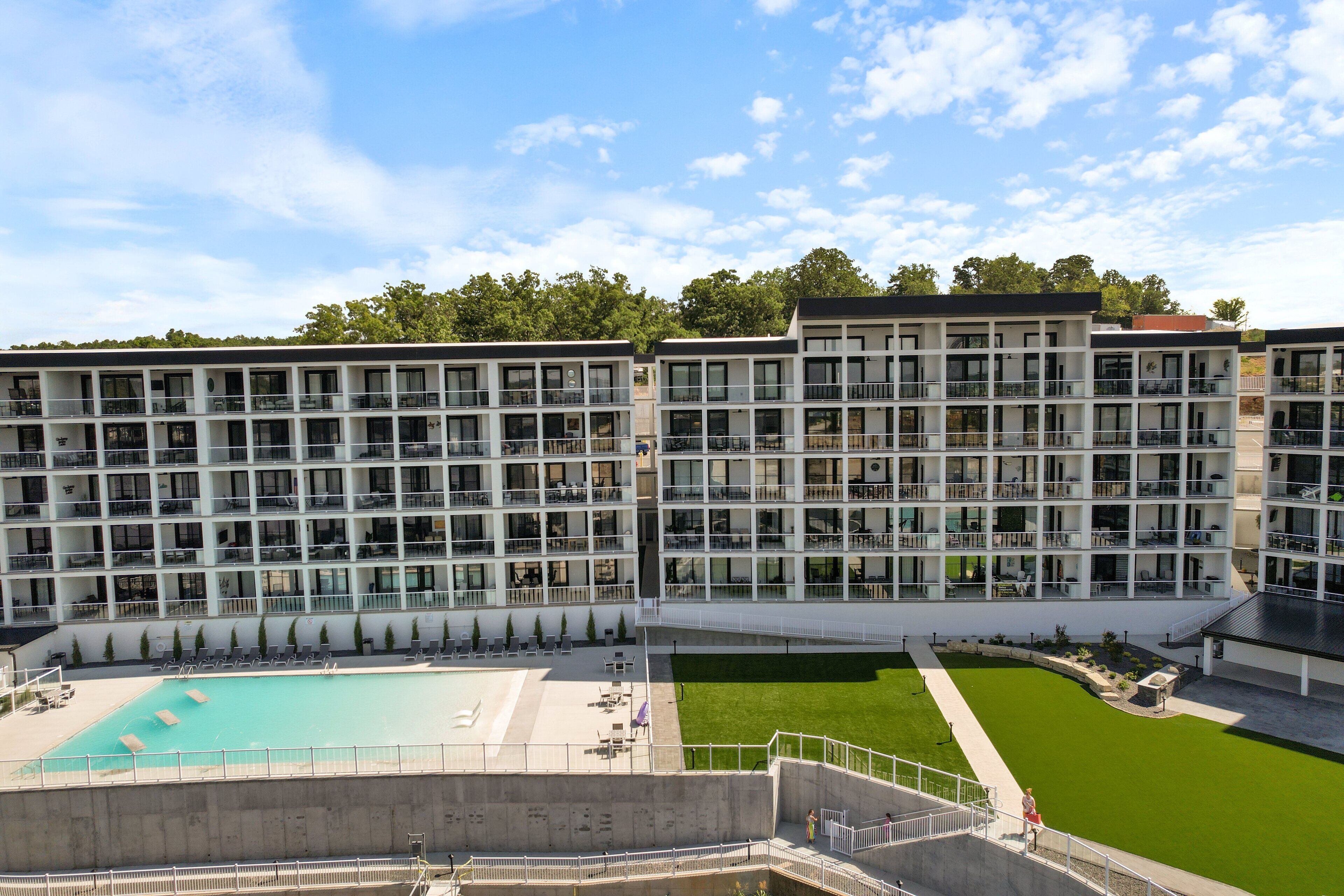 A multi-story hotel with a swimming pool and a green lawn area.