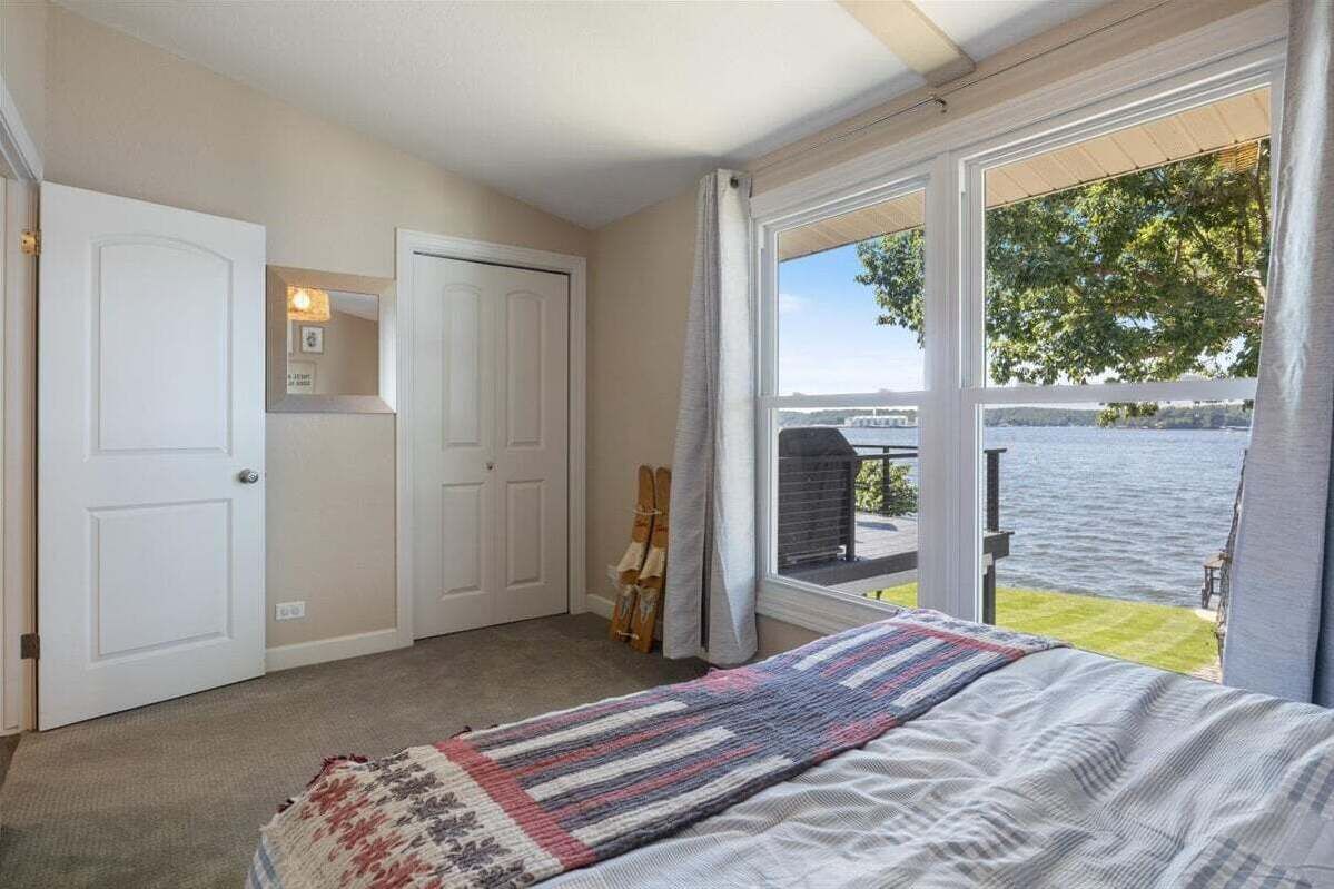 A bedroom with a large window overlooking a body of water, a bed with a striped blanket, and a door with a mirror and light fixture.