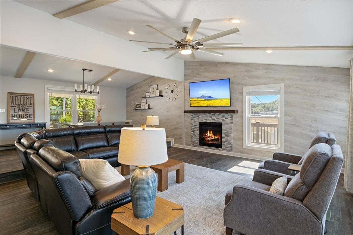 A spacious living room with a fireplace, a large flat-screen TV, and a ceiling fan.
