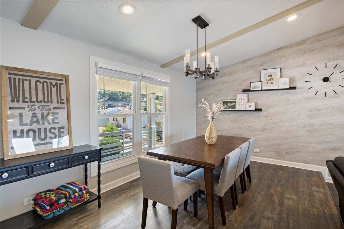 A dining area with a wooden table, grey upholstered chairs, a chandelier, and a wall clock.