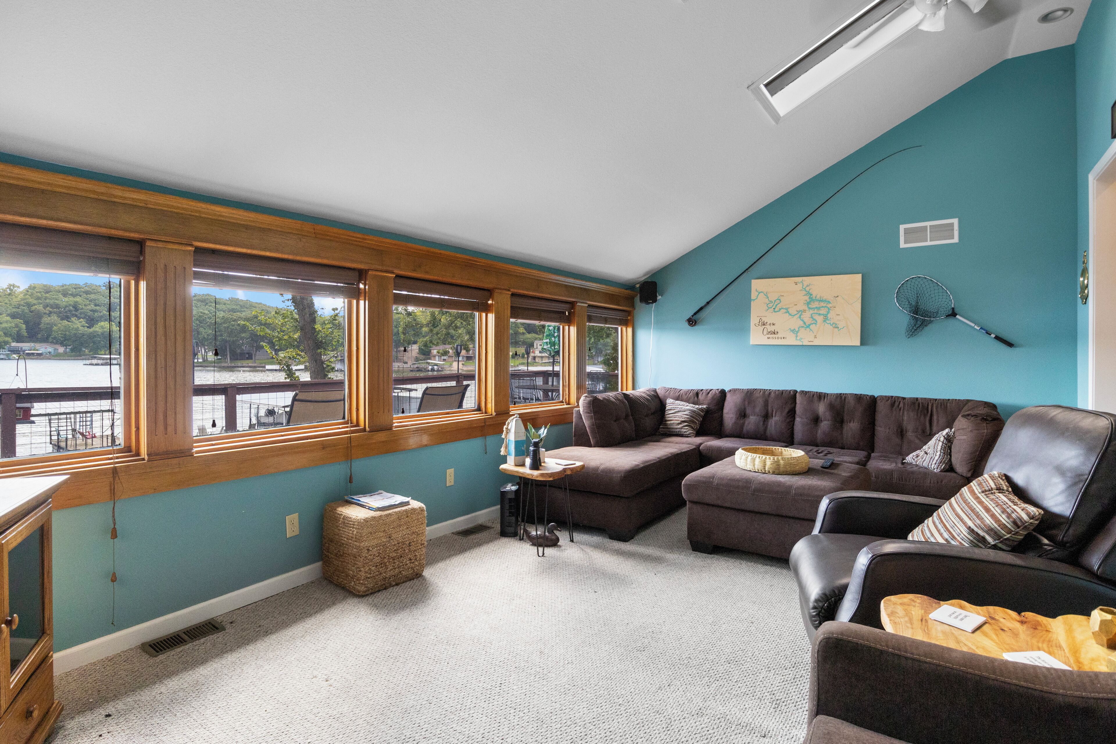 A living room with a sectional sofa, a small table, and a large window overlooking a body of water.