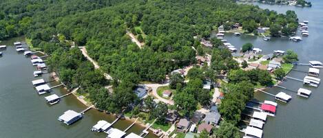 An aerial view of a lakeside property with multiple docked boats, surrounded by dense forest, and featuring a mix of residential and commercial buildings.