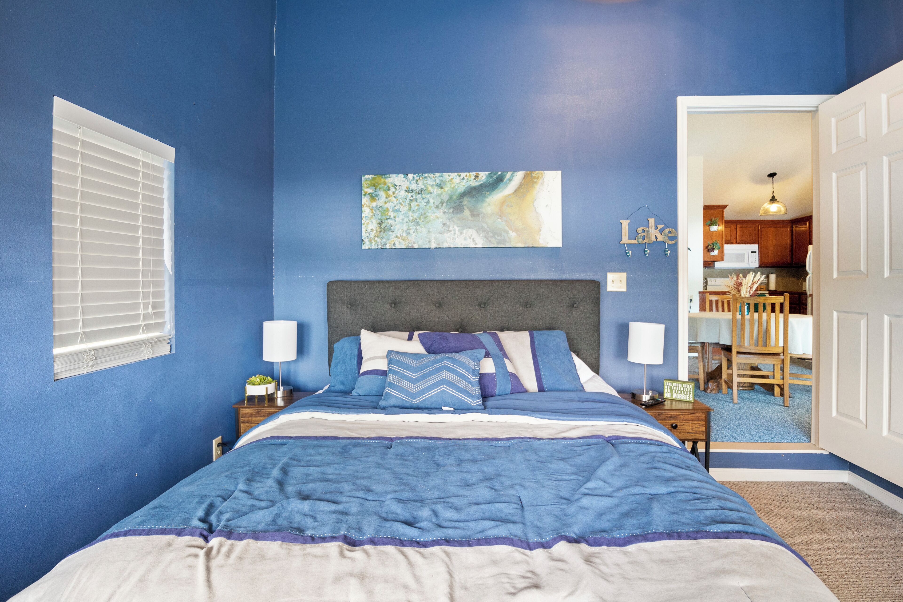 Une chambre à coucher avec un grand lit, une tête de lit, des tables de chevet et une fenêtre avec des stores.
