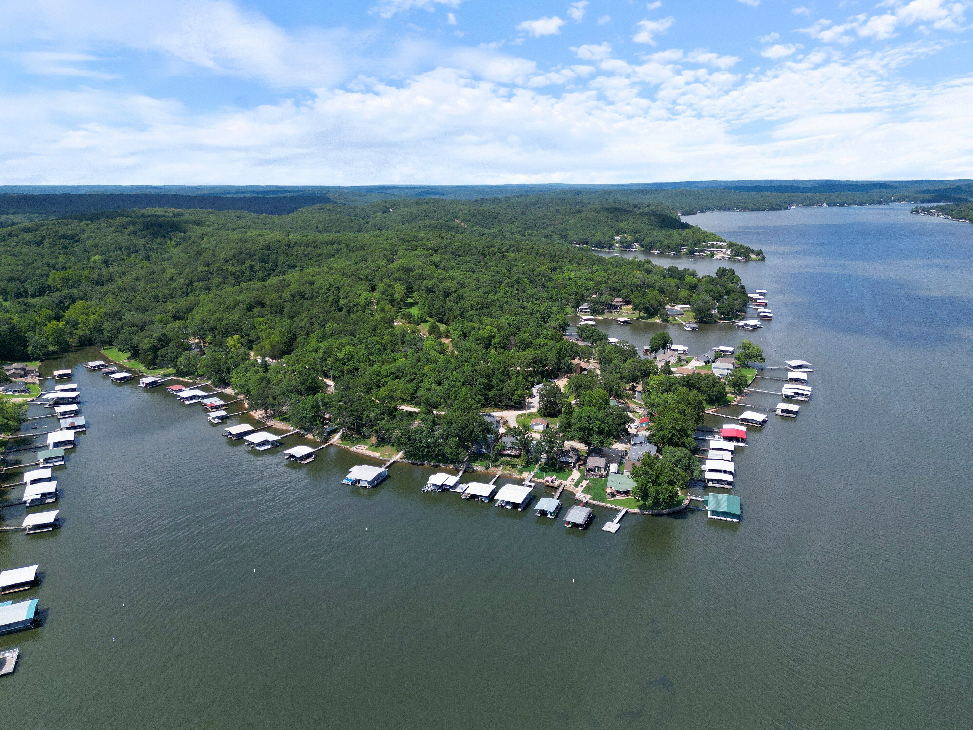 An aerial view of a lakeside property with numerous boats docked along the shore, surrounded by dense forest.
