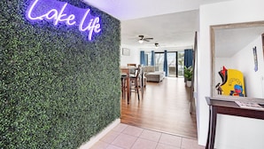 A modern living room with a neon sign reading "Lake Life," a dining area with wooden furniture, and a hallway leading to another room. - Treetop Vibes on Horseshoe Bend (Lake Ozark)