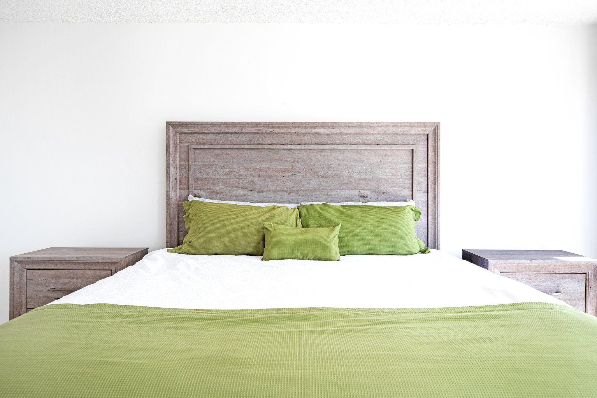 A bed with a wooden headboard, two green pillows, and a green blanket.