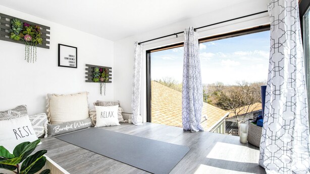 A modern room with a large window, a yoga mat, and decorative pillows with motivational phrases. - Treetop Vibes on Horseshoe Bend (Lake Ozark)