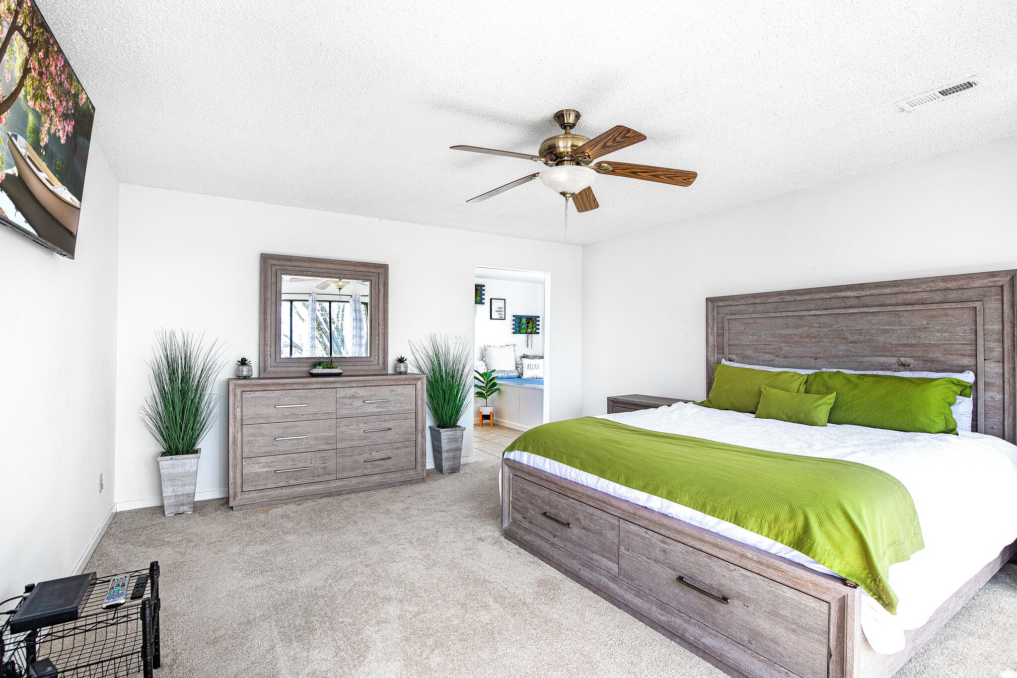 A bedroom with a wooden bed, green pillows, a ceiling fan, and a dresser.