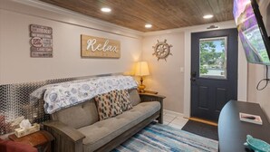 A cozy room with a sofa, a lamp, a wooden ceiling, a door, and a wall with a sign that says "Relax". - Lakefront Fishing Retreat w/ Dock, Hot Tub & Deck Views (Sunrise Beach)