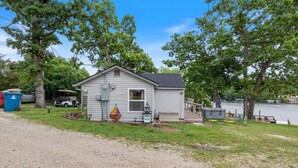 A small, single-story cabin with a porch, a small deck, and a dock extending into a body of water. - Lakefront Fishing Retreat w/ Dock, Hot Tub & Deck Views (Sunrise Beach)