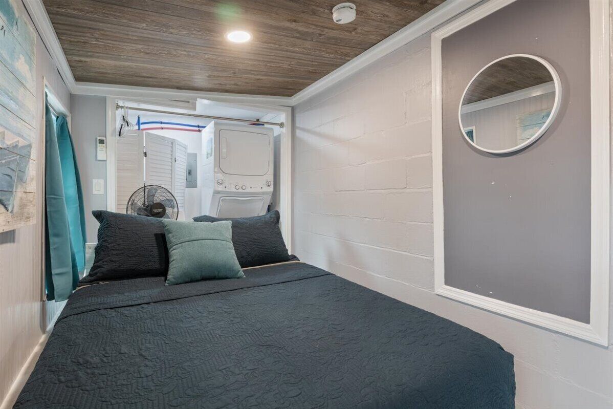 A bedroom with a bed, pillows, a round mirror, a ceiling fan, and a window with curtains.
