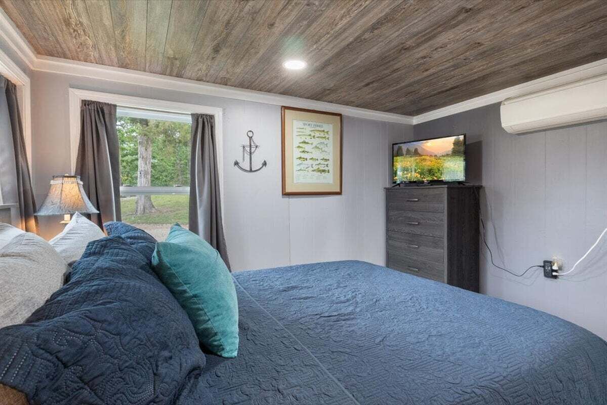 Un dormitorio con cama, televisor, un gráfico enmarcado de peces y una ventana con cortinas.