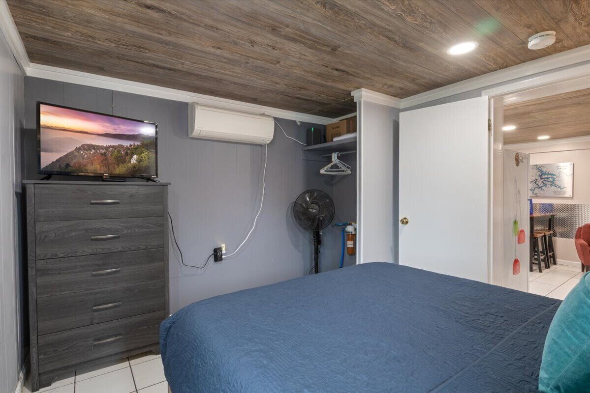 A bedroom with a bed, a dresser, a TV, and a fan.