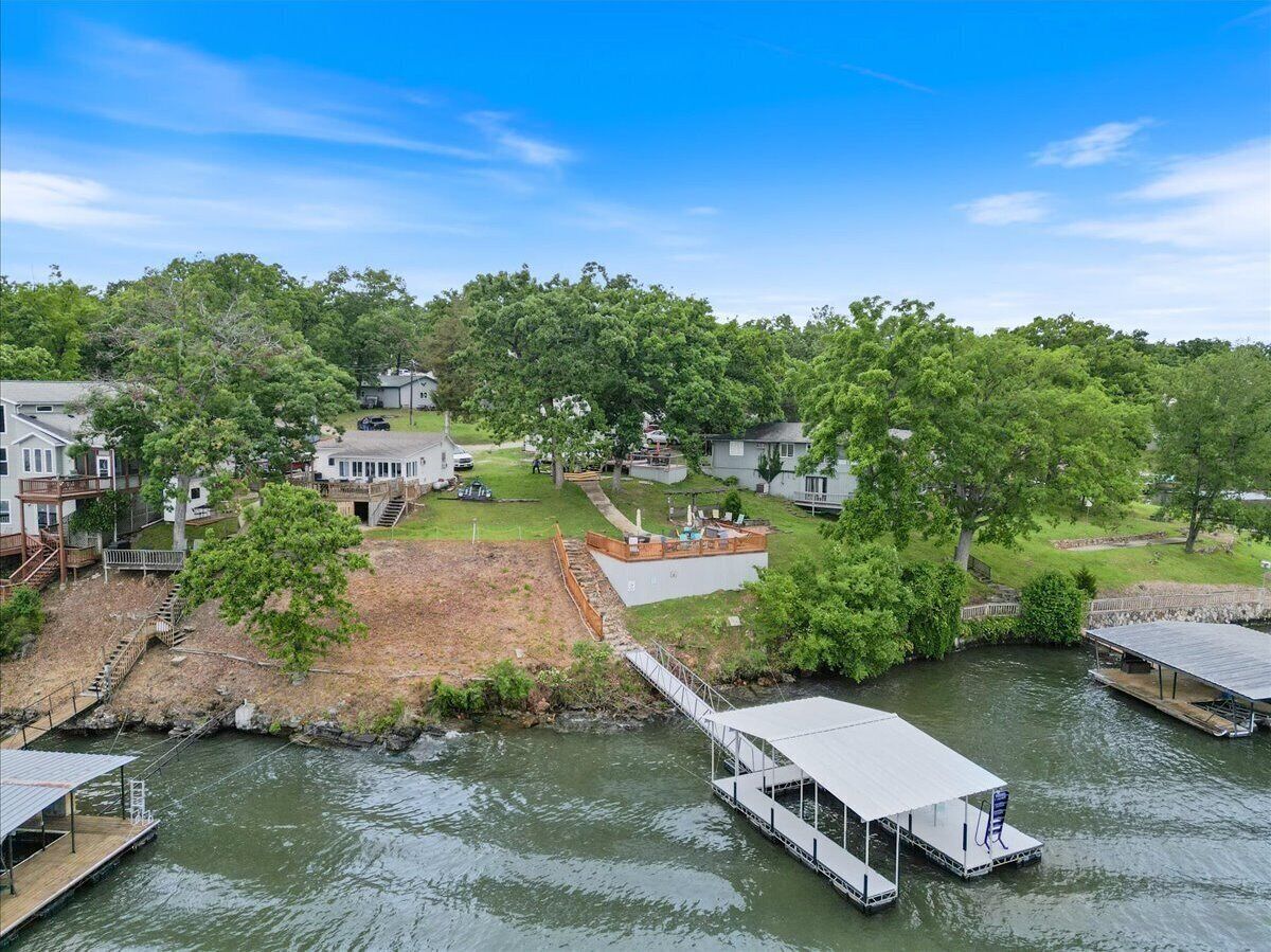A riverside property with a dock, a covered boat launch, and a grassy area with a staircase leading to a house.
