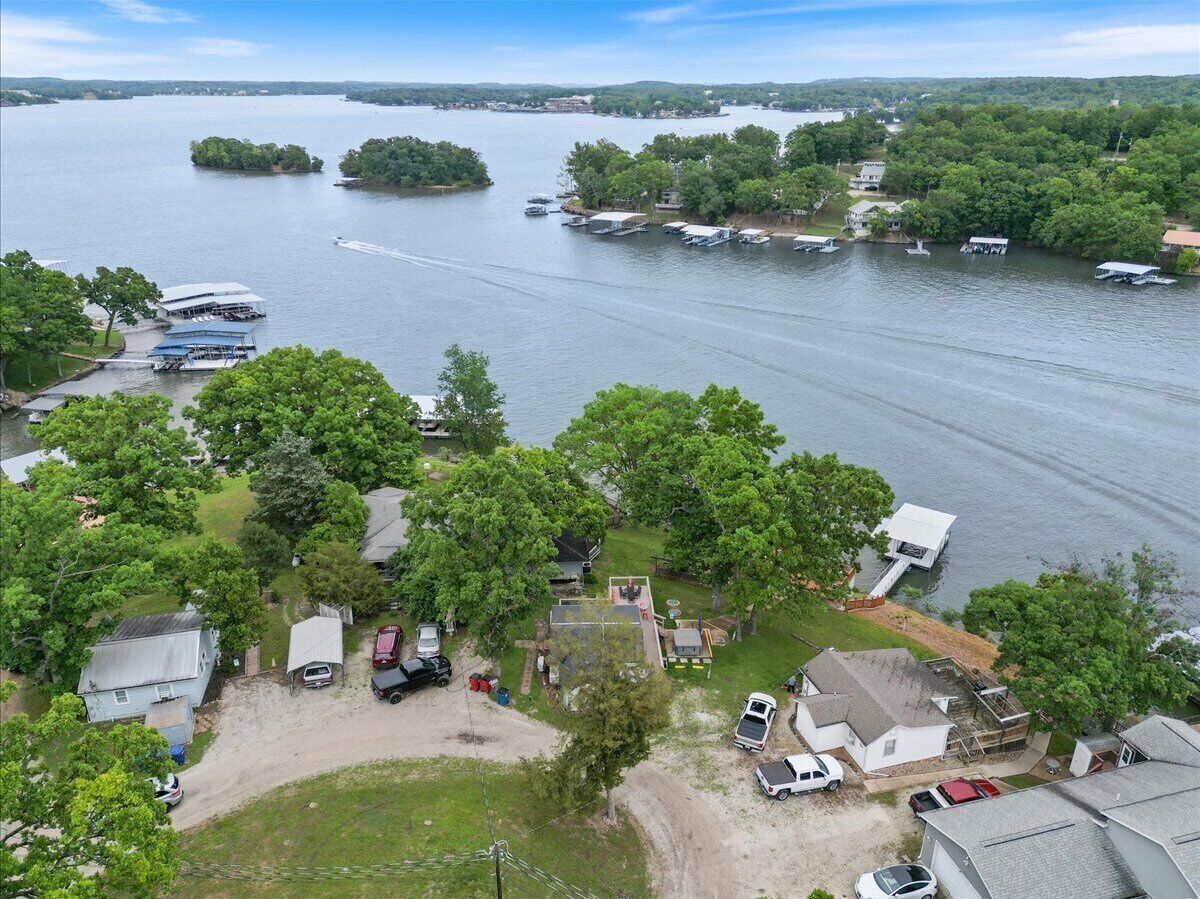 A lakeside property with multiple boats docked, a small dock, and several houses surrounded by trees.