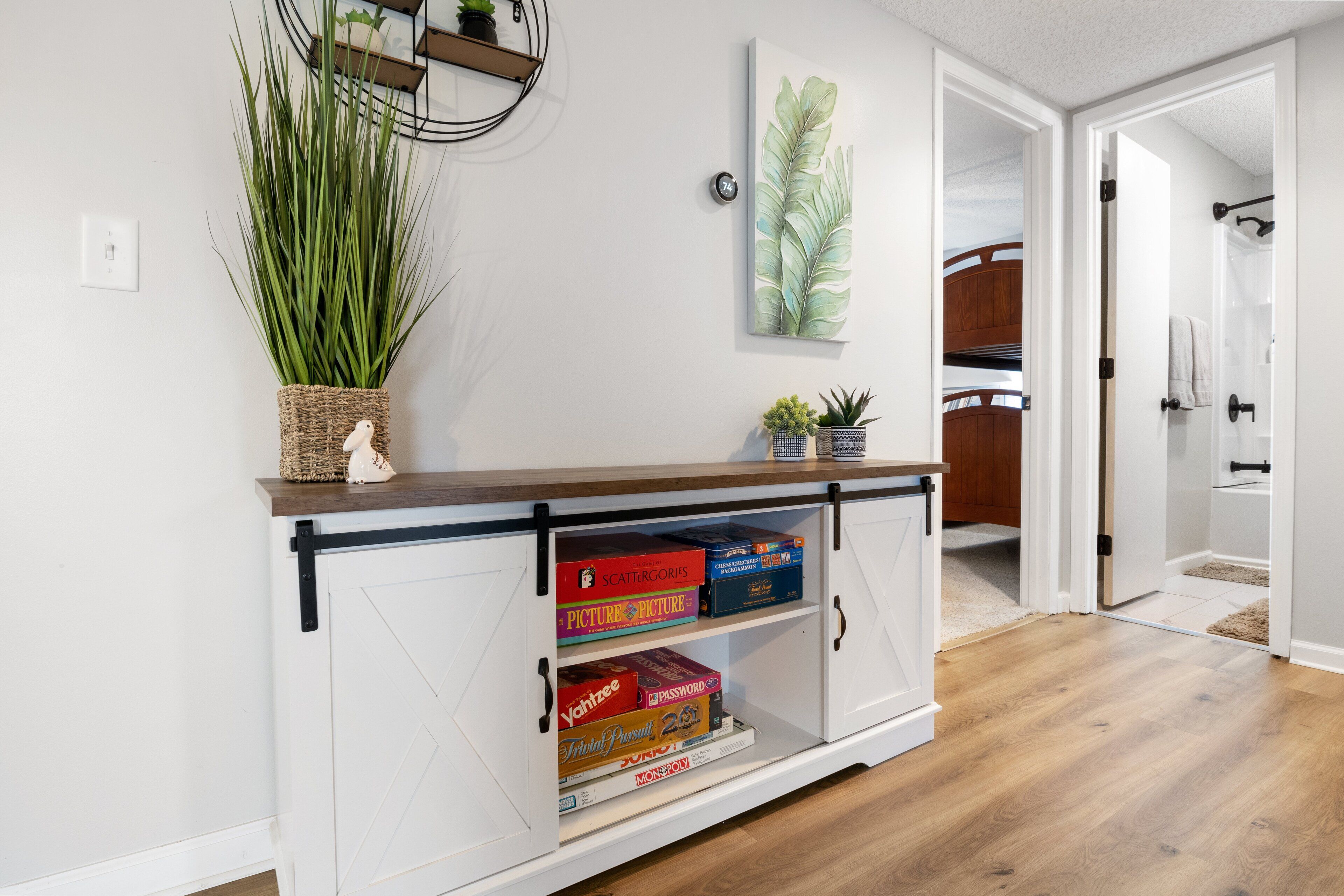 A white cabinet with black handles, a woven basket with a plant, and a framed leaf artwork on the wall.