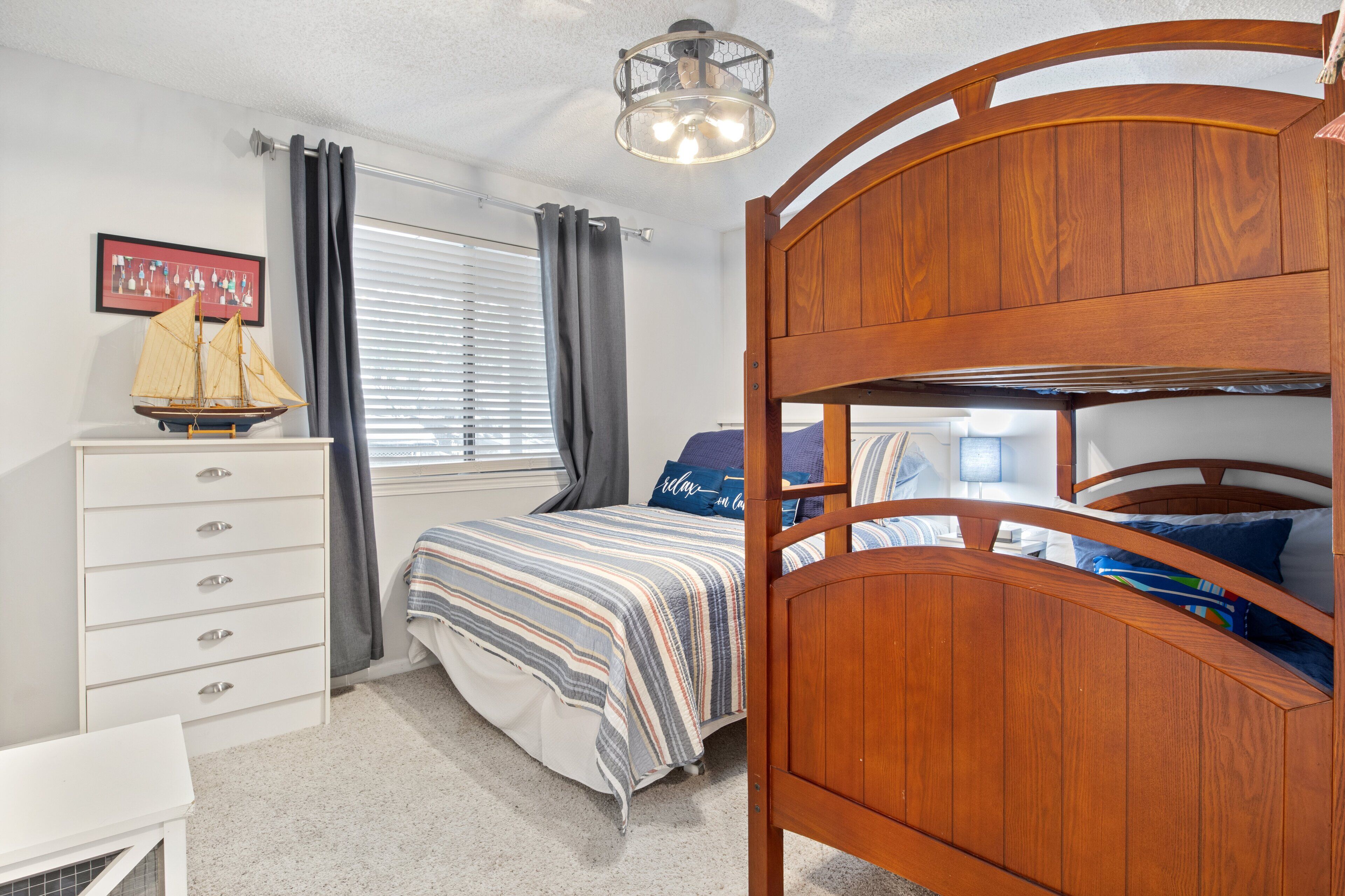A bedroom with a bunk bed, a dresser, a ship model, and a framed picture on the wall.