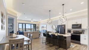A modern kitchen with a central island, bar stools, and a dining area with a wooden table and chairs. - Scenic Views, Outdoor Grill & Dine, Fireplace, Games (Osage Beach)