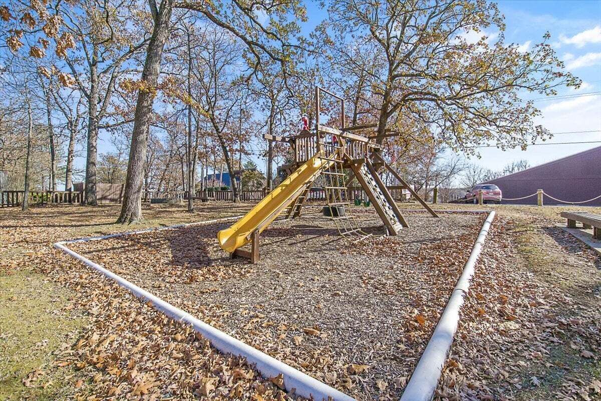 Un'area giochi con uno scivolo giallo e strutture per arrampicarsi, circondata da alberi e da un prato.