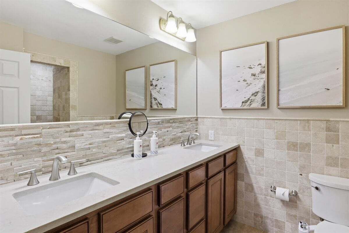 A bathroom with a white sink, two mirrors, a toilet, and a tiled backsplash.