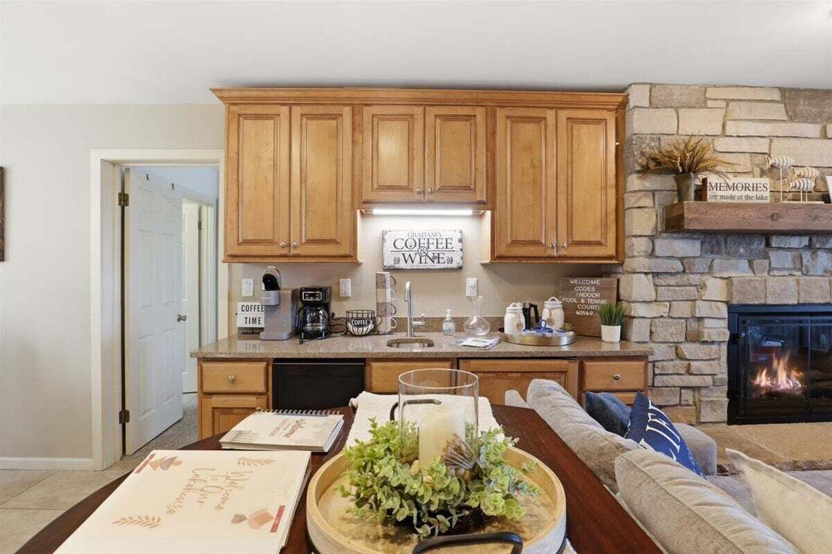 Una cocina con armarios de madera, una estación de café, una chimenea y un comedor con una mesa para dos.