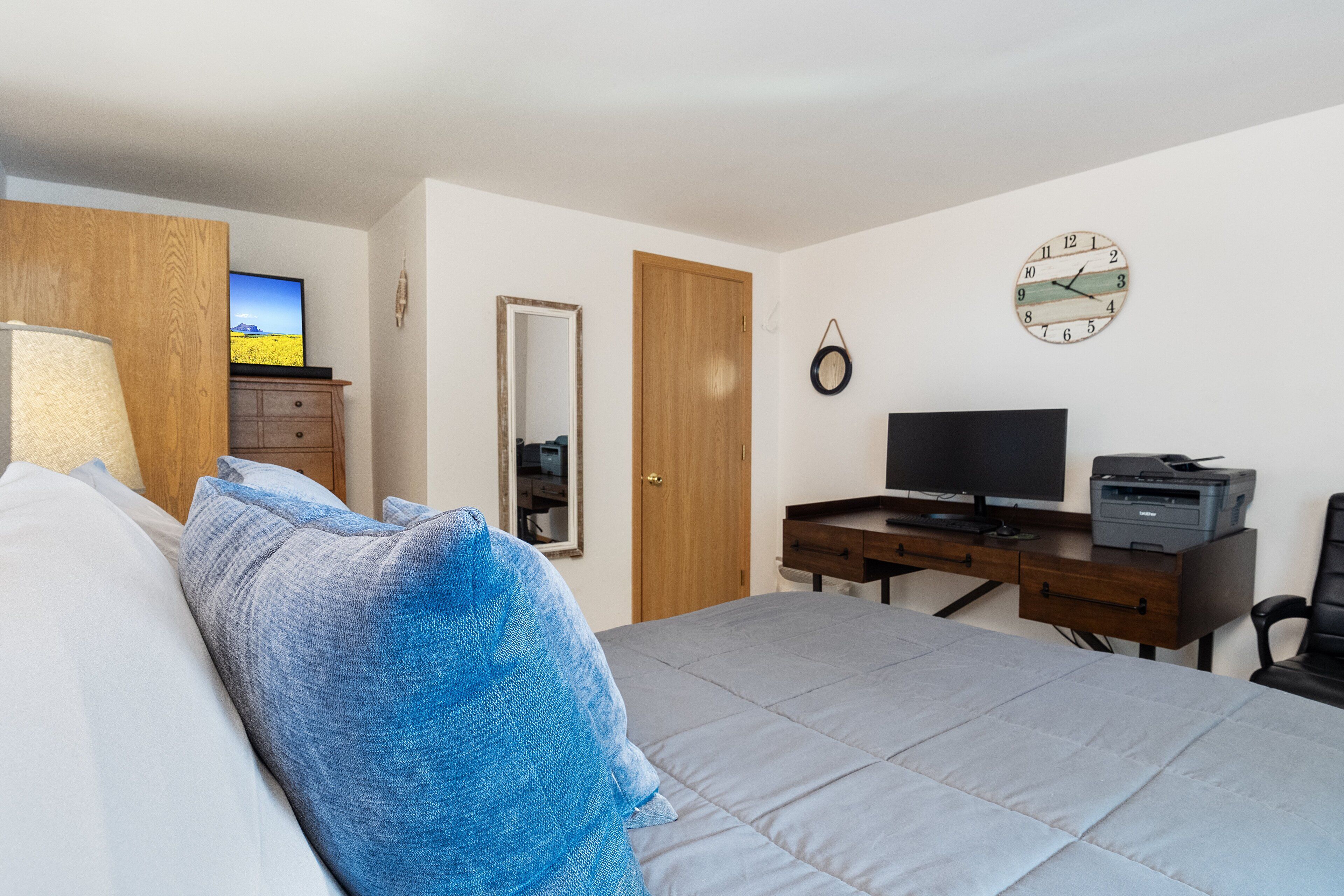 A bedroom with a bed, a desk with a computer, a television, and a clock on the wall.