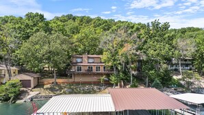 A dock with boats and a covered area, surrounded by trees and a house in the background. - Spacious, Quiet & Great Cove, Nearby Attractions, Private Dock, Fireplace, Expansive Deck (Rocky Mount)