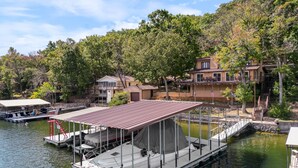 A dock with a covered boat area, a small boat, and a building with a balcony overlooking the water. - Spacious, Quiet & Great Cove, Nearby Attractions, Private Dock, Fireplace, Expansive Deck (Rocky Mount)