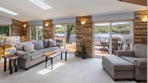 A spacious living area with a sofa, coffee table, and a view of a lake through large glass doors. - Spacious, Quiet & Great Cove, Nearby Attractions, Private Dock, Fireplace, Expansive Deck (Rocky Mount)