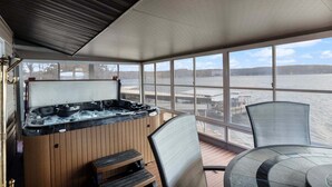 A covered outdoor area with a hot tub, wooden deck, and a table with chairs.