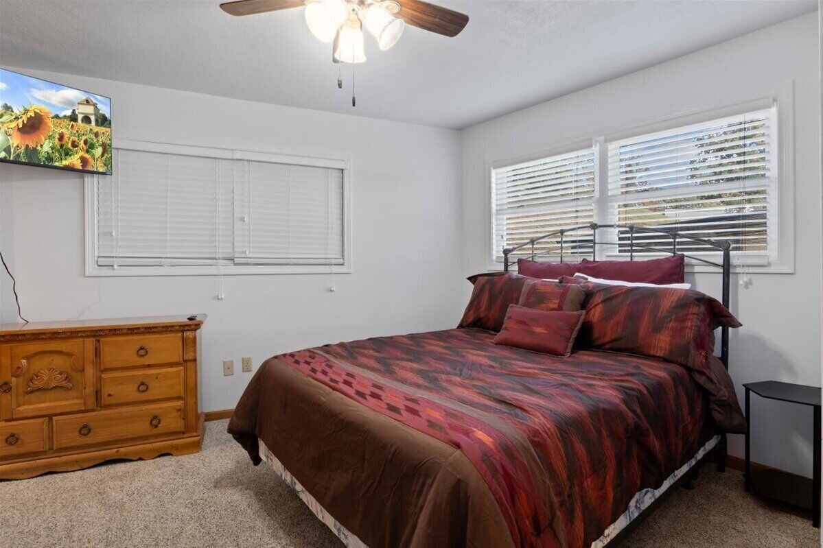Ein Schlafzimmer mit einem Bett, einer Holzkommode, einem Deckenventilator und einem an der Wand befestigten Fernseher.