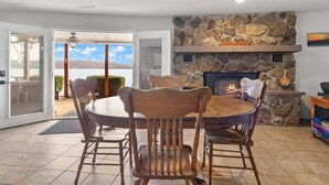 A dining area with a stone fireplace, wooden chairs, and a view of the outdoors.