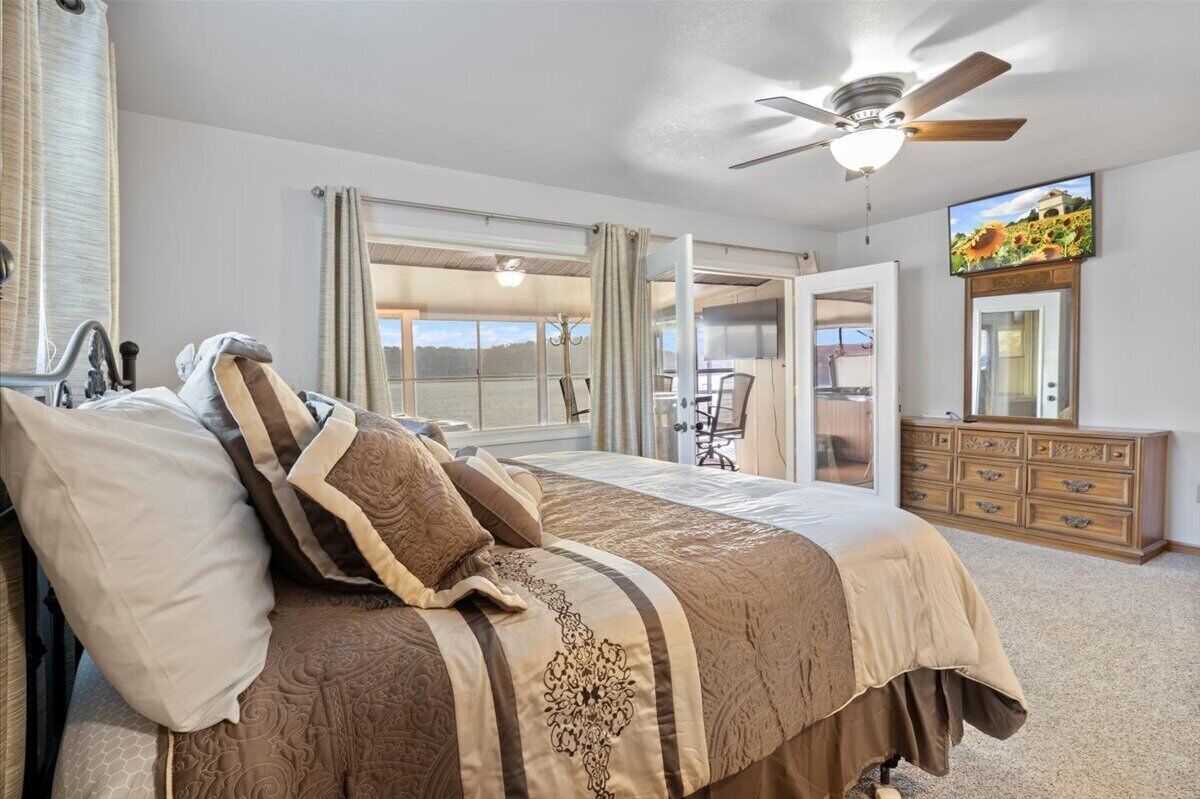 Une chambre à coucher comprenant un lit, un ventilateur de plafond, une commode et une grande fenêtre avec des rideaux.