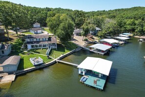 A lakeside property with docked boats, a covered boat house, and a small building. - Amazing Dock Fishing With Swim Area & Gentle Lot (Gravois Mills)