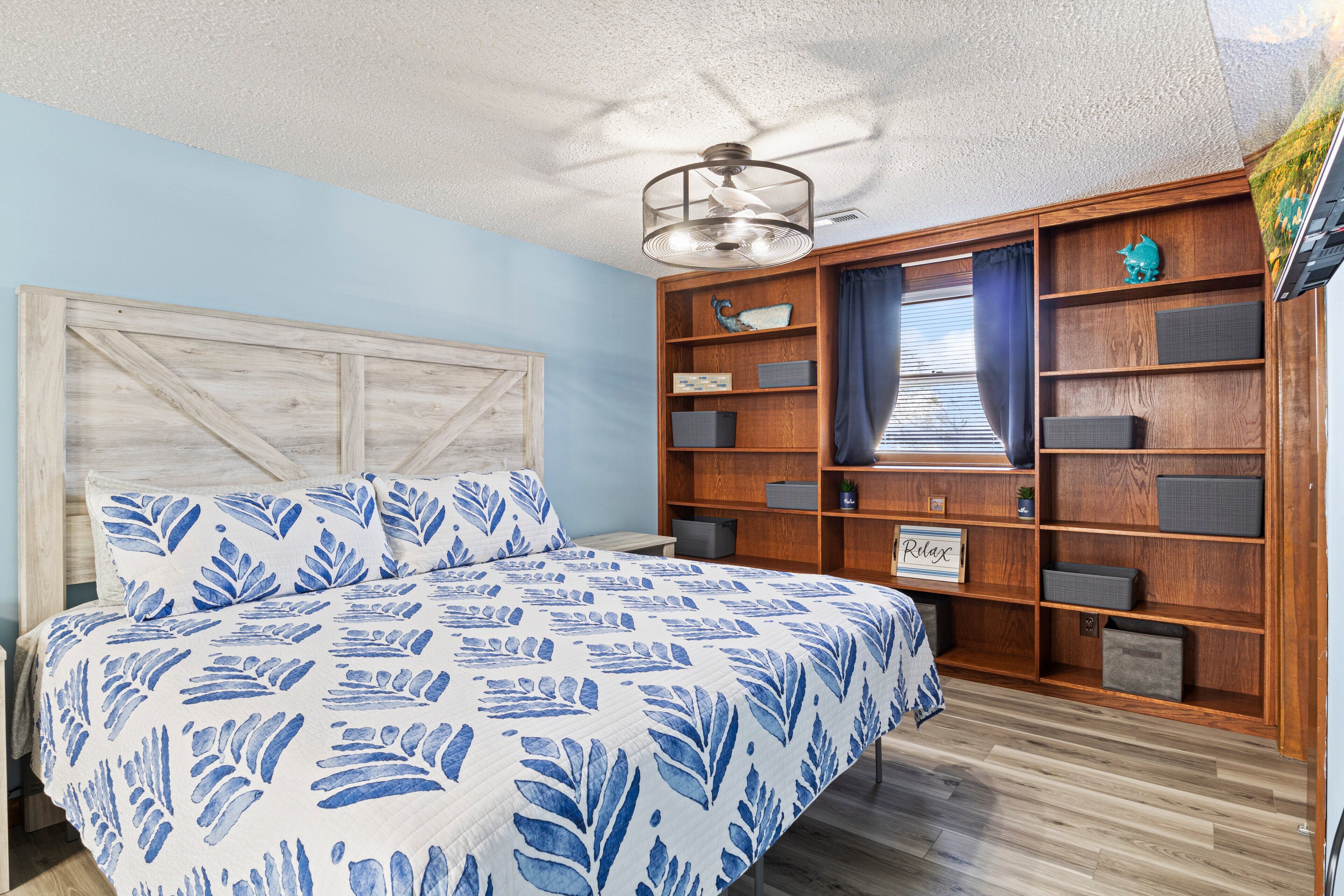 Une chambre à coucher avec un lit, une tête de lit en bois, des étagères intégrées et un ventilateur de plafond.