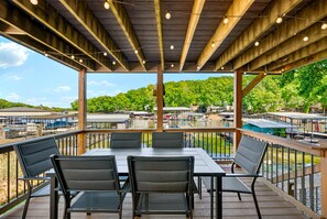 Un patio al aire libre con mesas y sillas, un muelle de madera y vistas a un lago y árboles.