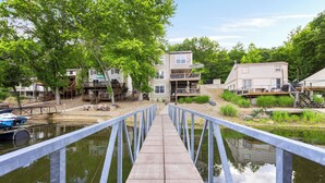 A wooden bridge leading to a waterfront area with buildings and a dock. - Newly Remodeled w/ Dock, Boat & PWC Slips, Pool Table & Golden Tee (Osage Beach)