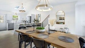 A modern kitchen with white cabinets, a wooden island, and a dining area with a long table and chairs. - Newly Remodeled w/ Dock, Boat & PWC Slips, Pool Table & Golden Tee (Osage Beach)