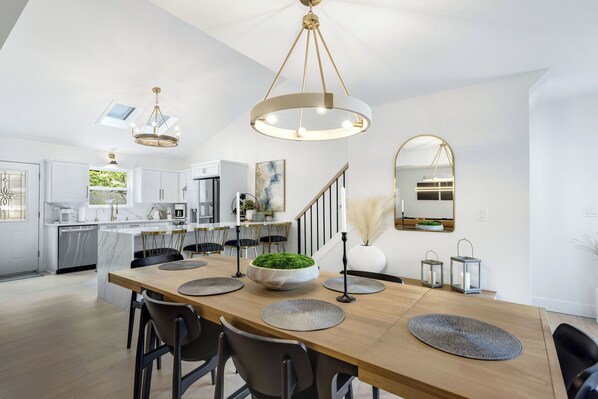 Una cocina moderna con armarios blancos, una isla de madera y un comedor con una mesa grande y sillas.