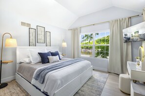 Un dormitorio moderno con una cama grande, lámparas de noche, televisión y vistas a zonas verdes por la ventana.