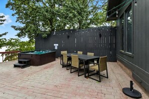 Une terrasse avec un jacuzzi, une table et des chaises, et une clôture sombre.