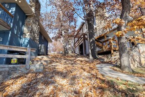A pathway surrounded by trees with autumn leaves, leading to a stone building with a wooden deck and a staircase. - Expansive Decks, Firepit, Stunning Views All Over (Gravois Mills)