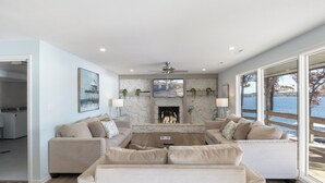 Ein modernes Wohnzimmer mit Kamin, zwei Sofas, einem Couchtisch und großen Fenstern mit Blick auf ein Gewässer.