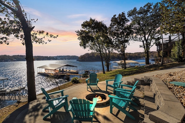 A lakeside deck with Adirondack chairs, a fire pit, and a view of the lake and dock. - Expansive Decks, Firepit, Stunning Views All Over (Gravois Mills)