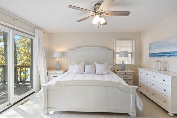 A bedroom with a large bed, a ceiling fan, a nightstand with a lamp, a dresser, and a window with blinds. - Expansive Decks, Firepit, Stunning Views All Over (Gravois Mills)