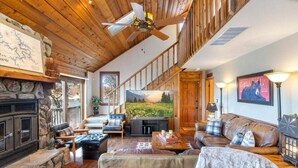 A cozy living room with a stone fireplace, wooden ceiling, and a large painting of a landscape.
