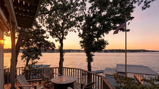 A deck with chairs and a table, overlooking a body of water with an American flag.