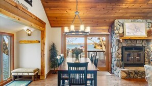 A dining area with a wooden table and chairs, a stone fireplace, and a view of the lake.