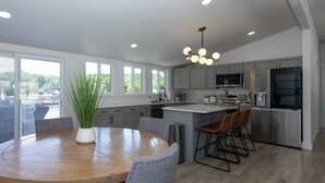 A modern kitchen with a central island, stainless steel appliances, and a view of the outdoors through large windows. - Great Location & Lake Views, Boat Slip (Lake Ozark)