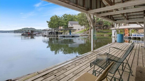 A wooden dock with a covered seating area overlooking a calm lake, boats docked, and houses in the background. - Lakefront Escape, Sunrise Views, Boat Slip & Community Dock Access (Roach)